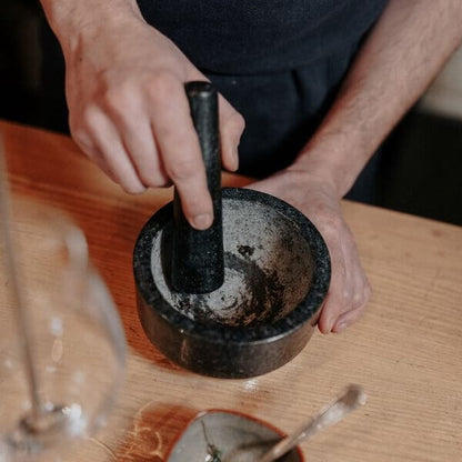 un cuisinier pilonne du poivre de kampot frais au sel dans un mortier en granit