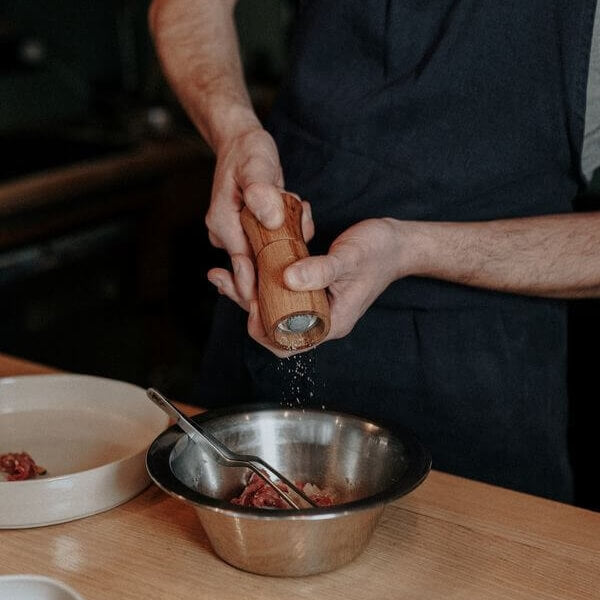 un chef de cuisine en train de moudre du poivre à l'aide d'un moulin en bois