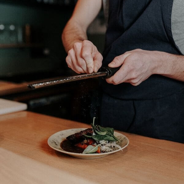 un chef cuisinier râpe du poivre long rouge au dessus d'une assiette de bœuf bourguignon à l'aide d'une râpe